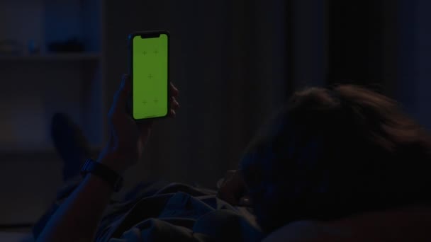 Homem Deitado Sofá Noite Segurando Smartphone Com Uma Tela Verde — Vídeo de Stock