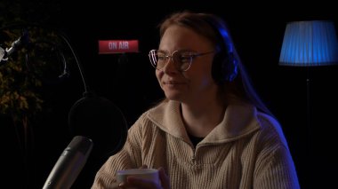 Güzel genç bayan DJ mikrofona konuşuyor, podcast 'i kaydediyor ya da radyo için gece haberlerini sunuyor. Podcast sunucusunun ya da DJ 'in mikrofondaki konuşmasını kapat. Profesyonel kulaklık takıyor..