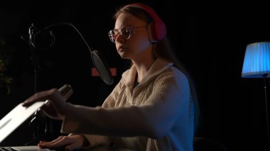 Güzel genç bayan DJ mikrofona konuşuyor, podcast 'i kaydediyor ya da radyo için gece haberlerini sunuyor. Podcast sunucusunun ya da DJ 'in mikrofondaki konuşmasını kapat. Profesyonel kulaklık takıyor..