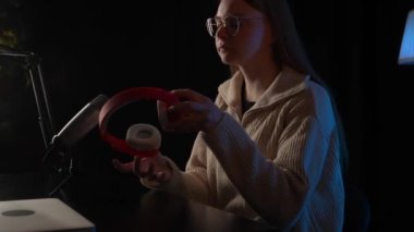 Güzel genç bayan DJ mikrofona konuşuyor, podcast 'i kaydediyor ya da radyo için gece haberlerini sunuyor. Podcast sunucusunun ya da DJ 'in mikrofondaki konuşmasını kapat. Profesyonel kulaklık takıyor..