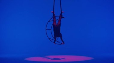 Ritmik jimnastikçi kız, metal bir yapı uydusunda tek koluyla havadaki pisliği canlandırıyor. Mavi arkaplan.