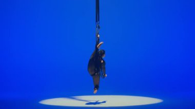 Ritmik jimnastikçi kız, metal bir yapı uydusunda tek koluyla havadaki pisliği canlandırıyor. Mavi arkaplan.