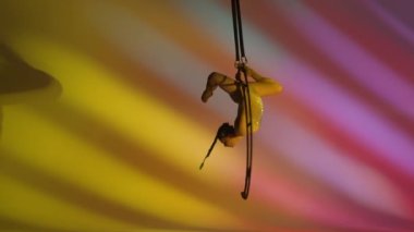 Ritmik jimnastikçi kız, metal bir yapı uydusunda tek koluyla havadaki pisliği canlandırıyor. Renkli arkaplan.