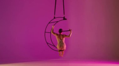 Ritmik jimnastikçi kız, bir kolu havada, metal bir yapının etrafında dönen pembe arka planda pislik yapıyor.