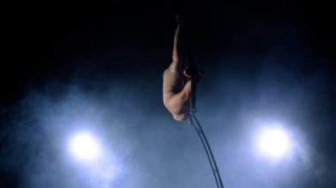 Ritmik jimnastikçi kız, metal bir yapı uydusunda tek koluyla havadaki pisliği canlandırıyor. Mavi dumanlı siyah arkaplan.