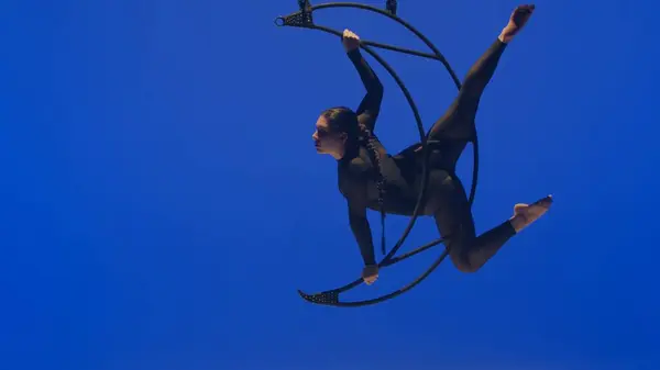 在一个金属旋转结构的月亮上 体操女子在空中的一只胳膊上表演人渣 蓝色背景 — 图库照片