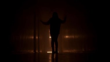 Siluet kadın karanlık bir koridor boyunca yürüyor. Turuncu ışık