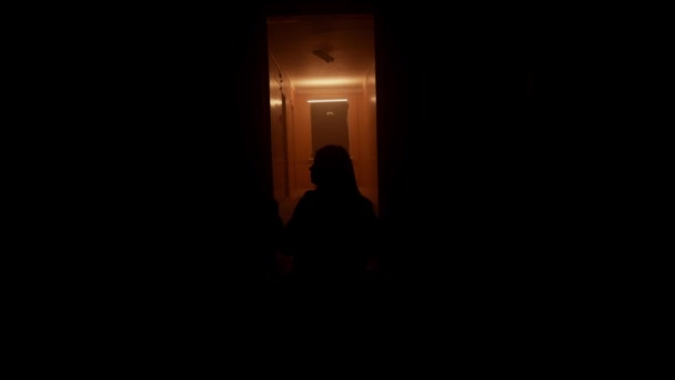 シルエットの女性は暗い廊下を歩いています 彼はドアを通って走っている オレンジライト — ストック動画