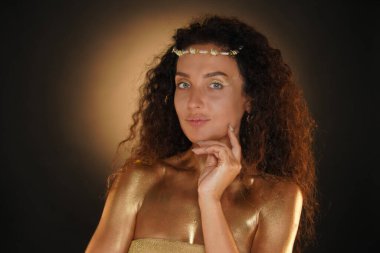 Güzellik ve cazibe yaratıcı reklam konsepti. Stüdyoda kadın modelin portresi. Taçlı, parlak makyajlı, altın sarısı makyajlı çekici bir kız kameraya bakıp yüzüne dokunuyor.