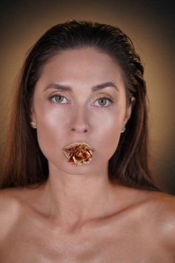 Güzellik ve moda yaratıcı reklam konsepti. Stüdyoda esmer kadın modelin portresi. Parlak göz makyajlı, altın gül çiçekli çekici bir kadın kameraya bakıyor..