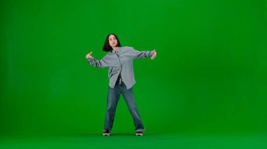 Çerçevede yeşil bir arka plan, bir topallama. Genç ve güzel bir kızla dans ediyor. Hip hop tarzında dans hareketleri gösteriyor. Kameraya dik dik bakıyor. Açık giyinmiş, sokak tarzı..