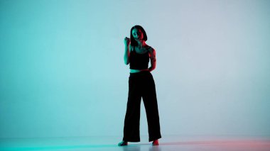 Mavi çerçeveli, açık arkaplanda. Genç ve güzel bir kızla dans ediyor. Hip hop tarzında dans hareketleri gösteriyor. Kameraya dik dik bakıyor. Siyah bluzlu ve pantolonlu bir kadın..