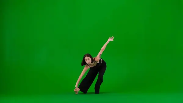 在绿色背景的框架里 一瘸一拐 舞姿年轻美丽的女孩展示嘻哈风格的舞蹈动作 她凝视着摄像机 她是个女人 光着脚穿着黑色上衣和裤子 — 图库照片