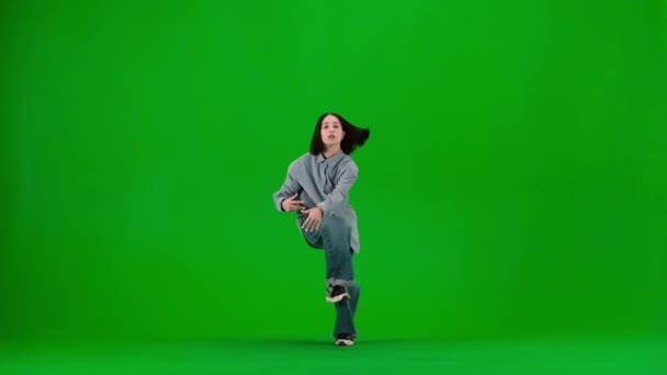 緑色の背景のフレームには スリップがあります 若くて美しい女の子を踊る ヒップホップのスタイルでダンスの動きを示しています カメラを見つめている影 ゆったりとした服装 ストリートスタイル — ストック動画