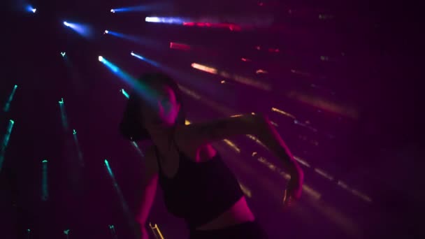 在镜头的黑暗背景上 彩虹光芒穿透了浓雾 形成了耀眼的光芒 这个女孩以嘻哈风格展示了舞蹈运动 她很有女人味 有节奏 — 图库视频影像