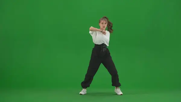 緑色の背景にあるフレームでは 染色体 若くて細く 美しい女の子が踊っている 彼女はジャズファンクの方向にさまざまなダンスの動きを示しています 彼女はリズム的でプラスチック的だ 一般プラン — ストック写真