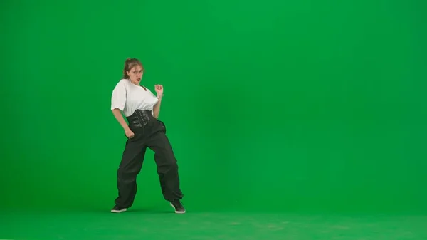 緑色の背景にあるフレームでは 染色体 若くて細く 美しい女の子が踊っている 彼女はジャズファンクの方向にさまざまなダンスの動きを示しています 彼女はリズム的でプラスチック的だ 一般プラン — ストック写真
