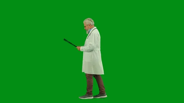 保健和健康创新概念 彩色键绿色屏幕上的演播室男医生画像 身穿白色制服的资深医生手握X光照片 一边走一边看 侧视图 — 图库照片