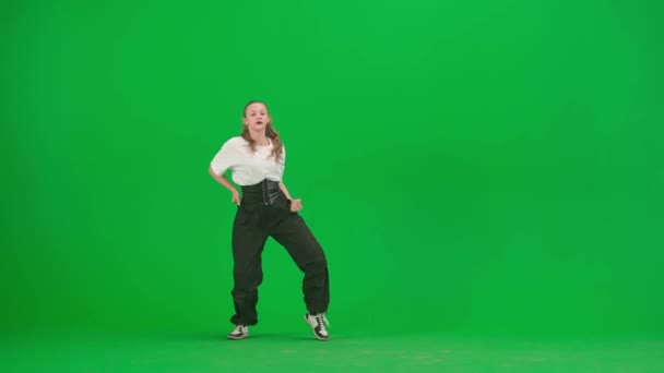 緑色の背景にあるフレームでは 染色体 若くて細く 美しい女の子が踊っている 彼女はジャズファンクの方向にさまざまなダンスの動きを示しています 彼女はリズム的でプラスチック的だ 一般プラン — ストック動画