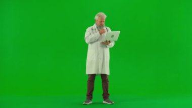 Sağlık ve tıbbi danışmanlık reklam konsepti. Krom anahtar yeşil ekranda yaşlı doktor portresi. Beyaz önlüklü kıdemli doktor dizüstü bilgisayarda duruyor, internetten bilgi okuyor..