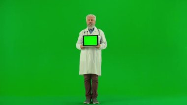 Sağlık ve tıbbi danışmanlık reklam konsepti. Krom anahtar yeşil ekranda yaşlı doktor portresi. Beyaz önlüklü kıdemli doktor elinde laptop, çalışma alanı modeli, kameraya gülümsüyor..