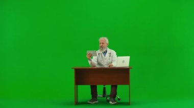Sağlık ve tıbbi danışmanlık reklam konsepti. Krom anahtar yeşil ekranda yaşlı doktor portresi. Bilgisayarlı kıdemli doktor hasta ile tablet görüntülü konuşma yapıyor..