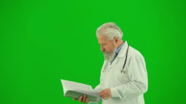 Sağlık ve tıbbi danışmanlık reklam konsepti. Krom anahtar yeşil ekranda insan sıhhiyesinin portresi. Beyaz önlüklü kıdemli doktor elinde tıbbi belgelerle yürüyor, okuyor..