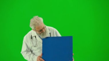 Sağlık ve tıbbi danışmanlık reklam konsepti. Krom anahtar yeşil ekranda insan sıhhiyesinin portresi. Beyaz önlüklü, elinde reklam panosu olan kıdemli doktoru kapat ve işaret et.