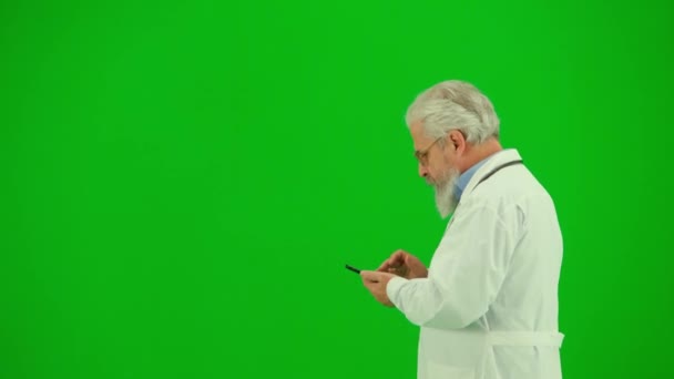 医療コンサルティング広告コンセプト クロマ グリーン スクリーンの男性の薬の肖像画 サイドビュー近いショットシニアドクター スマートフォンでテキストを歩く 情報を読む — ストック動画