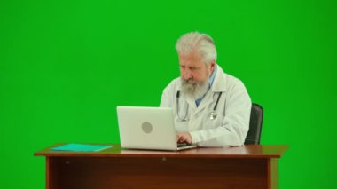 Sağlık ve tıbbi danışmanlık reklam konsepti. Krom anahtar yeşil ekranda insan sıhhiyesinin portresi. Üniformalı kıdemli doktoru kapat. Masada otur, dizüstü bilgisayarda çalış, bilgi yaz.