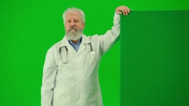 Sağlık ve tıbbi danışmanlık reklam konsepti. Krom anahtar yeşil ekranda insan sıhhiyesinin portresi. Üniformalı kıdemli doktor boş panonun yanında durup gülümsüyor..