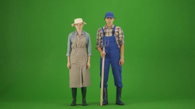 Tarım ve doğal tarım yaratıcı reklam kavramı. Krom anahtar yeşil ekranda çalışan çiftçi portresi. Bahçıvan adam ve kadın elinde yabayla kameraya poz veriyorlar..