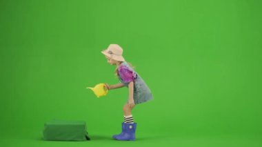 Bahçıvanlık ve tarım reklamları konsepti. Krom anahtar yeşil ekranda şapkalı ve lastik çizmeli bir kızın portresi. Küçük tatlı kız bahçıvan sulama bitkisi ve gülen surat..