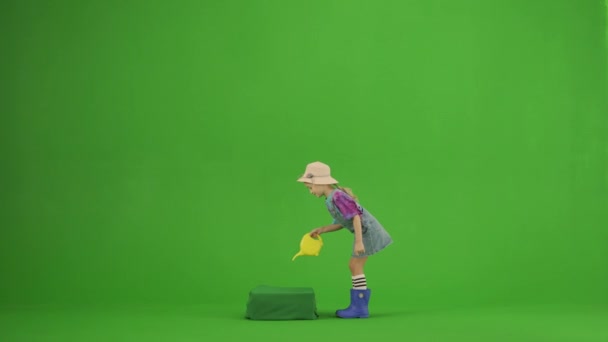 ガーデニングと農業の広告コンセプト クロマ グリーン スクリーンの帽子およびゴム製ブーツの少女の肖像画 小さなかわいいガールガーデナーウォータープラント黄色の小さな水やりができます — ストック動画