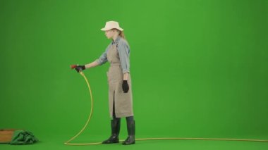 Bahçıvanlık ve tarım reklamları konsepti. Krom anahtar yeşil ekranda önlüklü kadın portresi ve lastik çizmeler. Bahçıvan kadın bahçe hortumuyla bitki yataklarını suluyor..