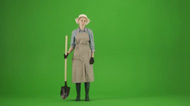 Bahçıvanlık ve tarım reklamları konsepti. Krom anahtar yeşil ekranda önlüklü kadın portresi ve lastik çizmeler. Kadın bahçıvan elinde kürekle etrafa bakıyor, yorgun yüz ifadesi..
