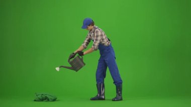 Bahçıvanlık ve tarım reklamları konsepti. Tulumlu erkek portresi ve krom anahtar yeşil ekranda lastik çizmeler. Bahçıvan adam su kabını alır ve bitkilerini sulamaya başlar..