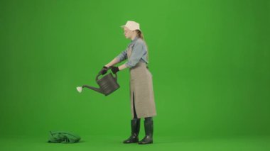 Bahçıvanlık ve tarım reklamları konsepti. Krom anahtar yeşil ekranda önlüklü kadın portresi ve lastik çizmeler. Bahçıvan kadın bahçe sulama tenekesi ve çiçekleri suluyor, gülümsüyor.