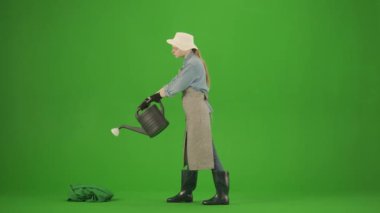 Bahçıvanlık ve tarım reklamları konsepti. Krom anahtar yeşil ekranda önlüklü kadın portresi ve lastik çizmeler. Kadın bahçıvan su bidonunu alıp bitkilerini sulamaya başlar..