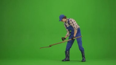 Bahçıvanlık ve tarım reklamları konsepti. Tulumlu erkek portresi ve krom anahtar yeşil ekranda lastik çizmeler. Bahçıvan adam eski bir tırpanla çimenleri biçiyor, pozitif görünüyor..