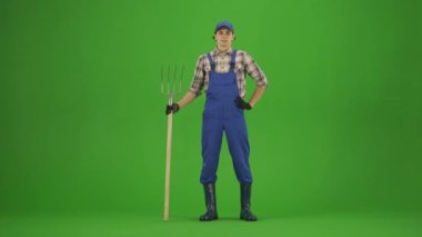 Bahçıvanlık ve tarım reklamları konsepti. Tulumlu erkek portresi ve krom anahtar yeşil ekranda lastik çizmeler. Erkek bahçıvan elinde yabayla durup bahçeye bakar..