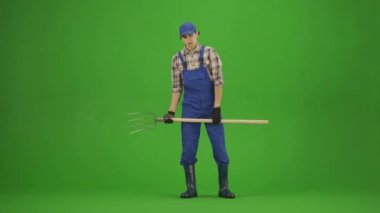 Bahçıvanlık ve tarım reklamları konsepti. Tulumlu erkek portresi ve krom anahtar yeşil ekranda lastik çizmeler. Bahçıvan elinde tırmıkla ayakta duruyor ve yorgun görünüyor..