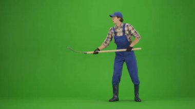 Bahçıvanlık ve tarım reklamları konsepti. Tulumlu erkek portresi ve krom anahtar yeşil ekranda lastik çizmeler. Erkek bahçıvan yabayla saman toplar, yorgun yüzünden ter siler..