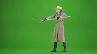 Bahçıvanlık ve tarım reklamları konsepti. Krom anahtar yeşil ekranda önlüklü kadın portresi ve lastik çizmeler. Kadın bahçıvan yabayla saman topluyor, yorgun yüzünden ter siliyor..