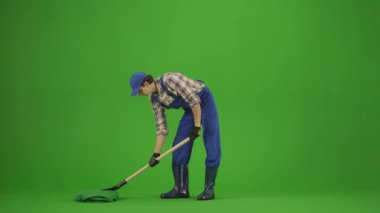 Bahçıvanlık ve tarım reklamları konsepti. Tulumlu erkek portresi ve krom anahtar yeşil ekranda lastik çizmeler. Bahçıvan bir ağaç dikmiş ve kökleri kürekle kaplamış..