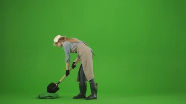 Bahçıvanlık ve tarım reklamları konsepti. Krom anahtar yeşil ekranda önlüklü kadın portresi ve lastik çizmeler. Kadın bahçıvan bir ağaç dikmiş ve kökleri kürekle kaplamış..