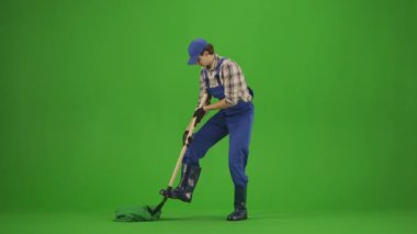 Bahçıvanlık ve tarım reklamları konsepti. Tulumlu erkek portresi ve krom anahtar yeşil ekranda lastik çizmeler. Bahçıvan adam kürekle toprak kazıyor, kafasını sallıyor..
