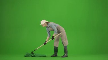 Bahçıvanlık ve tarım reklamları konsepti. Krom anahtar yeşil ekranda önlüklü kadın portresi ve lastik çizmeler. Kadın bahçıvan, çapayla zemini gevşetiyor, olumlu bir ifade..