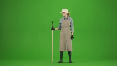 Bahçıvanlık ve tarım reklamları konsepti. Krom anahtar yeşil ekranda önlüklü kadın portresi ve lastik çizmeler. Kadın bahçıvan elinde çapayla kameraya bakıp gülümsüyor..