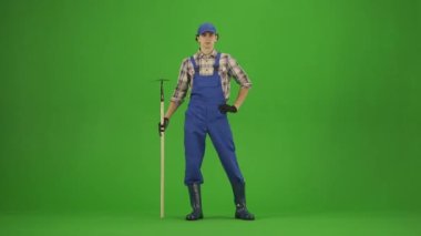 Bahçıvanlık ve tarım reklamları konsepti. Tulumlu erkek portresi ve krom anahtar yeşil ekranda lastik çizmeler. Bahçıvan adam elinde çapayla durur ve bahçeye bakar..